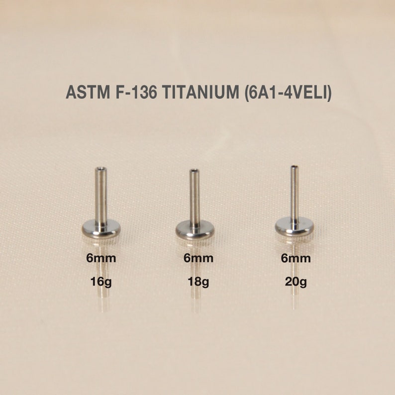 May include: Three titanium body jewelry pieces, each with a 6mm length and a flat disc base. The pieces are shown in 16 gauge, 18 gauge, and 20 gauge sizes. The text "ASTM F-136 TITANIUM (6A1-4VELI)" is displayed above the jewelry.