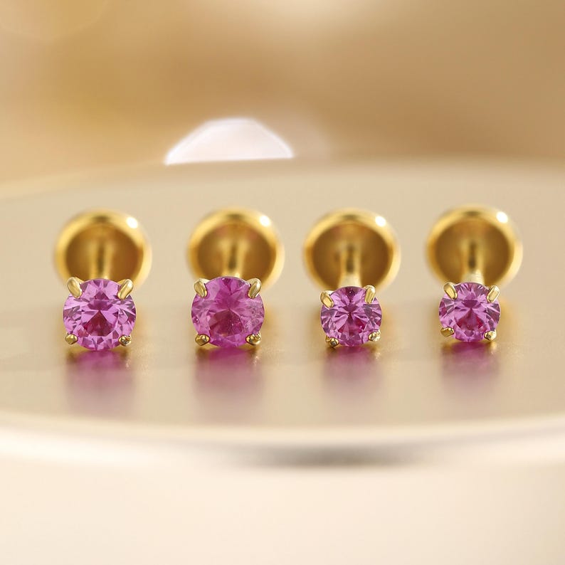 K&ouml;nnte beinhalten: Vier goldfarbene Ohrstecker mit runden, leuchtend pinkfarbenen Edelsteinen. Die Ohrringe sind in einer Reihe angeordnet und zeigen die lebendige Farbe der Edelsteine und die polierte Goldfassung. Die Ohrringe sind klein und zart.