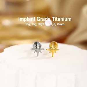 May include: Two star-shaped stud earrings, one silver-toned and one gold-toned, featuring an eight-pointed design. Text on the image reads: Implant Grade Titanium, 16g, 18g, 20g / 5, 6, 7, 8, 10mm. These studs have a flat back post for secure wear.