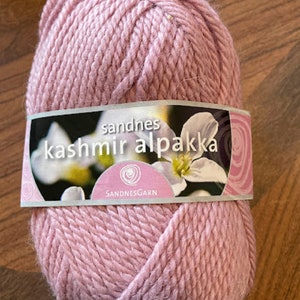 May include: A ball of pink Sandnes Kashmir Alpaca yarn. The label reads "Sandnes Kashmir Alpaca" with a flower graphic.