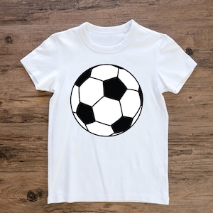 May include: White t-shirt with a black and white football design. The football graphic is centrally placed and features black pentagons and white hexagons, outlined in black. The shirt has short sleeves and a crew neck.