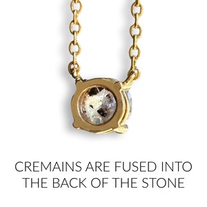 May include: A gold chain necklace with a round pendant. The back of the pendant is clear and contains cremains. The text "CREMAINS ARE FUSED INTO THE BACK OF THE STONE" is below the pendant.