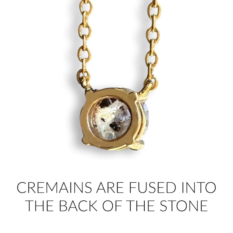 May include: A gold chain necklace with a round pendant. The back of the pendant is clear and contains cremains. The text "CREMAINS ARE FUSED INTO THE BACK OF THE STONE" is below the pendant.