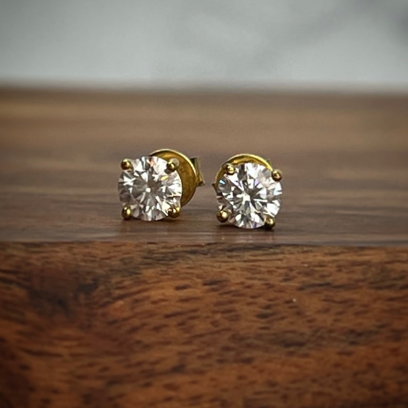 May include: A pair of gold stud earrings with round, clear cubic zirconia stones.