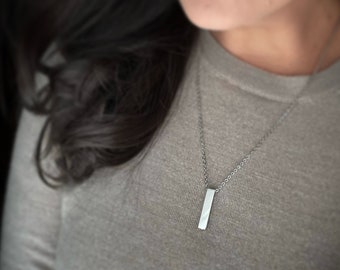 May include: A silver necklace with a thin chain and a long, rectangular pendant.