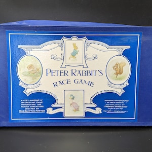 Puede incluir: Caja azul con un juego de mesa Peter Rabbit's Race Game. La caja presenta ilustraciones de Peter Rabbit, Jemima Puddle-Duck, Squirrel Nutkin y Mr. Jeremy Fisher. El texto en la caja dice "Peter Rabbit's Race Game" y "Un juego muy divertido e interesante que presenta a los famosos personajes creados por Miss Beatrix Potter."