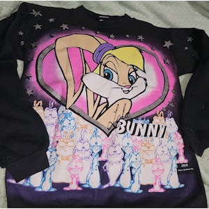 May include: Black long-sleeved sweatshirt with a graphic of Lola Bunny in a pink heart. The word "BUNNY" is printed below the heart, with cartoon bunnies at the bottom. The top of the sweatshirt has a star pattern.