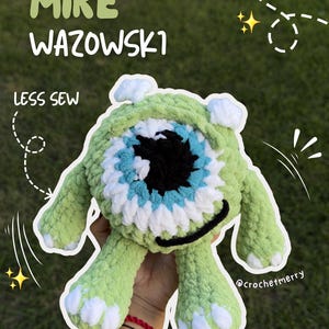 May include: A green crocheted plush toy featuring a large central eye with a black pupil, blue iris, and white sclera. The character has two small white horns, two arms, and two legs with white accents. Text reads MIKE WAZOWSKI and LESS SEW.