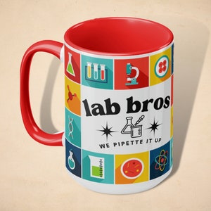 Puede incluir: Taza de cerámica blanca con interior rojo y un diseño colorido con iconos relacionados con la ciencia. La taza tiene un asa negra y el texto "lab bros we pipette it up".