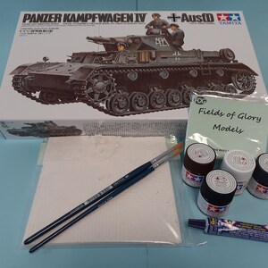 May include: A model kit of a German Panzerkampfwagen IV tank with Ausf D, along with paint, brushes, and glue. The box art features a detailed illustration of the tank with soldiers on top. The box is labelled "Tamiya" and "Fields of Glory Models".