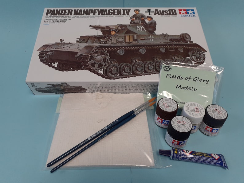 May include: A model kit of a German Panzerkampfwagen IV tank with Ausf D, along with paint, brushes, and glue. The box art features a detailed illustration of the tank with soldiers on top. The box is labelled "Tamiya" and "Fields of Glory Models".