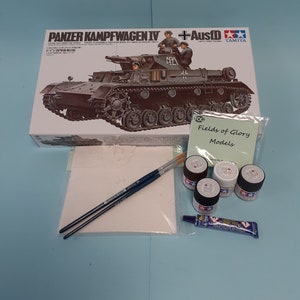 May include: A model kit of a German Panzerkampfwagen IV tank with a +Ausf D designation. The box art features a detailed illustration of the tank with soldiers in military uniforms. The kit is made by Tamiya.
