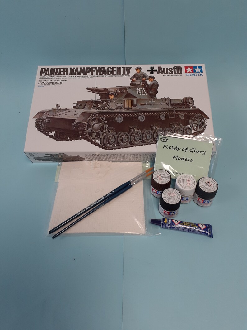 May include: A model kit of a German Panzerkampfwagen IV tank with a +Ausf D designation. The box art features a detailed illustration of the tank with soldiers in military uniforms. The kit is made by Tamiya.