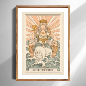 May include: A framed tarot card print featuring the Queen of Cups. The artwork depicts a regal figure with a crown, holding a golden chalice, seated on a throne amidst stylized waves. The color palette includes soft blues, golds, and creams.