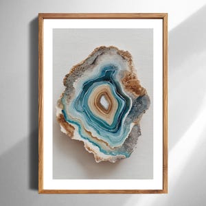 May include: A framed print of a geode slice, showcasing concentric layers of blue, brown, and white hues. The artwork is set against a white background and framed in a natural wood frame, creating a decorative piece.