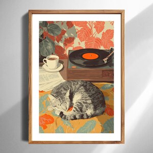 Könnte beinhalten: Ein gerahmter Kunstdruck mit einer gemütlichen Szene mit einer schlafenden Tabby-Katze auf einer Oberfläche mit floralem Muster. Ein Plattenspieler, eine Tasse Kaffee und eine Zeitung sind ebenfalls zu sehen. Der Hintergrund hat ein florales Tapetendesign.
