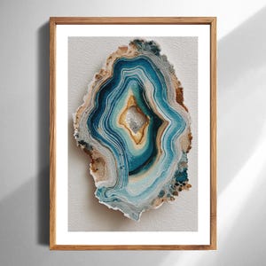 Puede incluir: Una impresión en acuarela enmarcada de una rebanada de geoda. La obra de arte presenta bandas concéntricas de azul, turquesa, marrón y beige, que se asemejan a la piedra natural. La impresión está enmarcada en un marco de madera marrón claro, adecuado para la decoración del hogar.