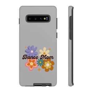 May include: A grey phone case with a floral design and the text "Dance Mom." The flowers are in shades of purple, orange, yellow, and green, with star accents. The case has a sleek, modern design.