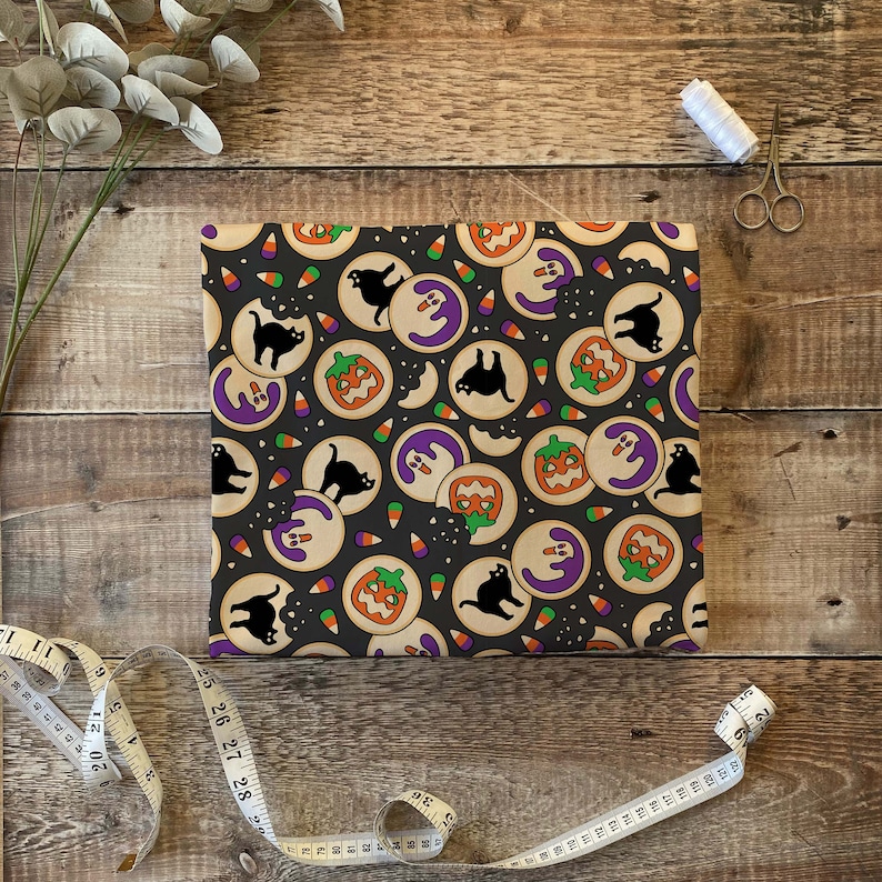 Puede incluir: Tela de tem&aacute;tica de Halloween negra y naranja con un patr&oacute;n repetido de galletas, gatos y ma&iacute;z dulce. Las galletas est&aacute;n decoradas con glaseado morado y tienen un mordisco. Los gatos son negros y el ma&iacute;z dulce es naranja y amarillo.