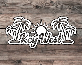 May include: A white Key West sign with palm trees and a sun design, set against a wooden background. The text "Key West" is in a stylized font, evoking a tropical theme.