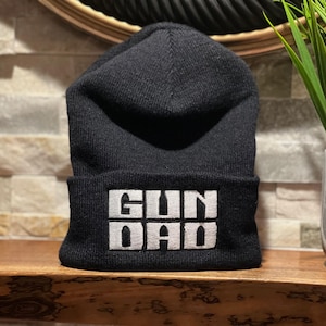 May include: Black beanie with a white embroidered design that says "GUN DAD".