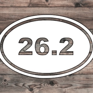 May include: White oval sign with a double border on a wood background. The sign says "26.2" in a large, bold font.