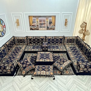 Könnte beinhalten: Eine traditionelle marokkanische Sitzgruppe mit einem schwarzen und goldenen Musterstoff. Die Sitzgruppe umfasst mehrere Kissen und einen niedrigen Tisch. Die Kissen sind in U-Form mit einem kleinen Tisch in der Mitte angeordnet.