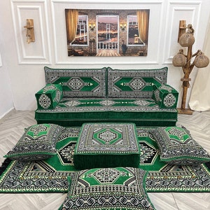 Puede incluir: Un juego de sofás con estampado verde y negro con cojines y alfombra a juego. El juego incluye un sofá, una otomana cuadrada y varias almohadas cuadradas. La alfombra y los cojines tienen flecos negros.