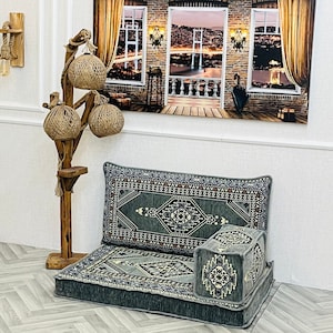 May include: A set of floor cushions with a traditional geometric pattern in shades of blue, gray, and white. The cushions are arranged in a seating configuration, with a smaller cushion placed in front of a larger one. The cushions are on a wood floor with a herringbone pattern.