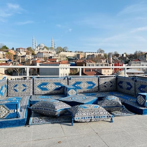 Puede incluir: Una zona de asientos con estampado azul y blanco con cojines y almohadas en una terraza en la azotea con vistas a un horizonte urbano con una mezquita en la distancia.
