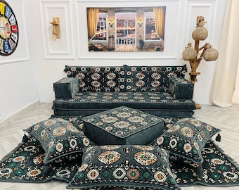 May include: A dark green and brown patterned sofa with matching floor cushions and a square ottoman. The sofa and cushions have a traditional design with tassels. The ottoman has a geometric pattern.