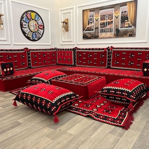May include: A red sectional sofa with matching pillows and a rug. The sofa and pillows have black and white patterned accents. The room also features a large clock and artwork.