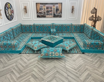 May include: A teal blue and cream patterned floor seating set with a square ottoman and four square pillows. The set is arranged in a U-shape on a light gray wood floor.