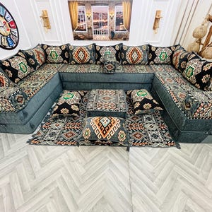 May include: A large, U-shaped sofa set with patterned cushions and a matching rug. The cushions and rug feature a geometric design in black, orange, green, and white. The sofa is a muted teal colour, creating a cohesive living room set.