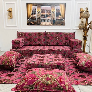 Könnte beinhalten: Ein rosa und braunes, gemustertes Sofa mit passenden Bodenkissen und einem kleinen quadratischen Ottoman. Das Sofa besteht aus mehreren Kissen und ist im traditionellen Stil gehalten.