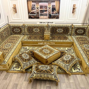 Peut inclure: Un grand canapé d'angle orné avec des coussins assortis et un ottoman central. Le canapé et les coussins présentent un motif floral doré et marron. La zone d'assise mesure 190 cm de long et 70 cm de profondeur. L'épaisseur de l'assise est de 20 cm.