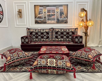 May include: A maroon and patterned living room set featuring a sofa, two ottomans, and several throw pillows. The set includes a matching rug and a small coffee table. The room is decorated with a painting and a wooden lamp.