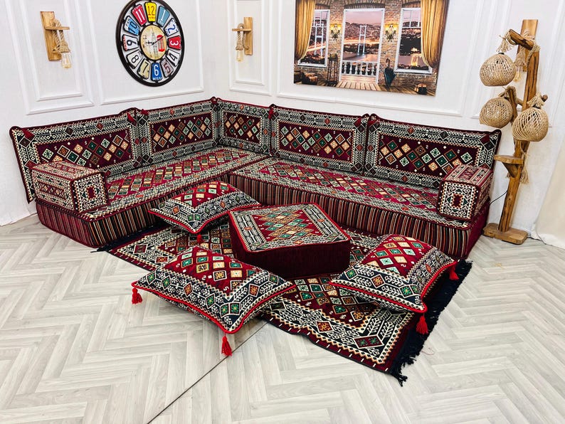 May include: A traditional red and gold patterned divan with matching cushions and throw pillows. The divan is set on a patterned rug with a decorative clock on the wall behind it.