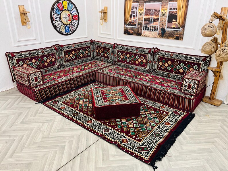 May include: A red and gold patterned divan with a matching patterned rug and a red and gold patterned ottoman. The divan is made up of multiple cushions and has a fringe border.