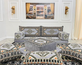 May include: A gray and black patterned floor cushion set with a large gray floor cushion in the center. The set includes four smaller cushions and a gray ottoman.