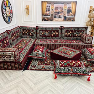 May include: A red and green patterned floor cushion set with a matching rug. The cushions are arranged in a sectional shape and include a variety of sizes and shapes. The rug has a geometric pattern and is made of a soft, plush material.