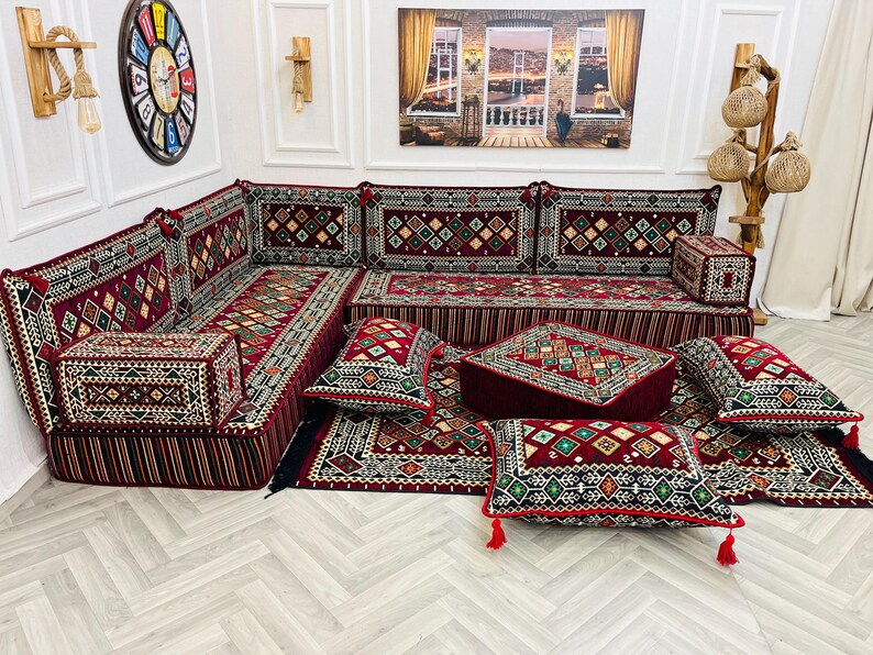 May include: A red and green patterned floor cushion set with a matching rug. The cushions are arranged in a sectional shape and include a variety of sizes and shapes. The rug has a geometric pattern and is made of a soft, plush material.