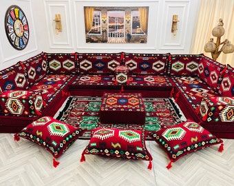 May include: A red and white patterned floor cushion set with a matching rug and coffee table. The cushions are arranged in a U-shape and feature intricate geometric designs.