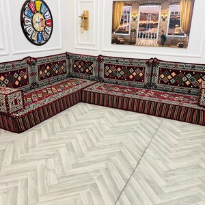May include: A traditional red and gold patterned floor seating set with a corner design. The set features multiple cushions with intricate embroidery and a deep red base.