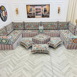 May include: A gray and white patterned sectional sofa with multiple cushions and a matching ottoman. The sofa is arranged in a U-shape and is set on a light gray wood floor.