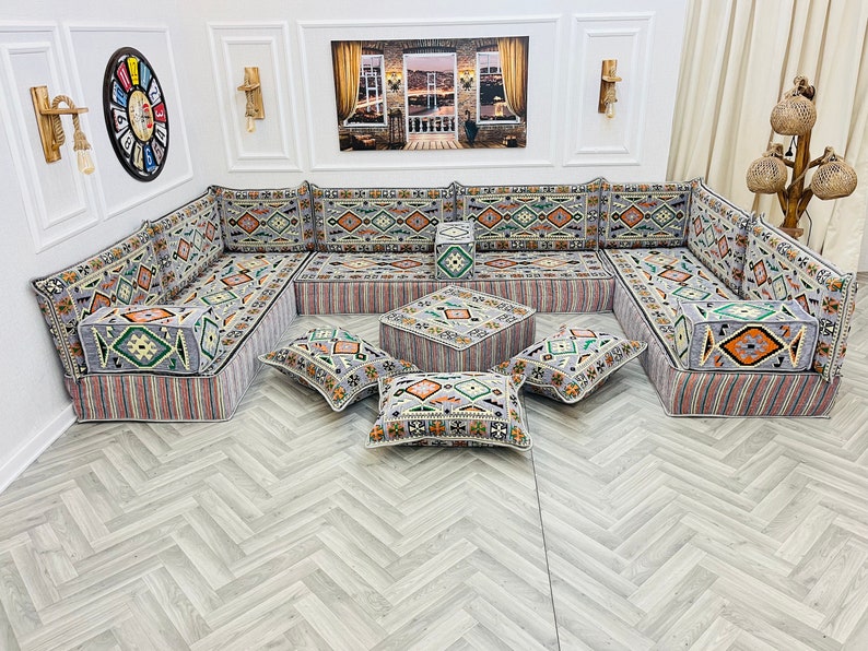 May include: A gray and white patterned sectional sofa with multiple cushions and a matching ottoman. The sofa is arranged in a U-shape and is set on a light gray wood floor.