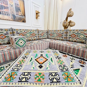 May include: A gray and white patterned sectional sofa with orange and green accents. The sofa is made up of multiple cushions and is arranged in a U-shape. There are three gray and white patterned throw pillows on the sofa. The sofa is sitting on a gray and white patterned rug.