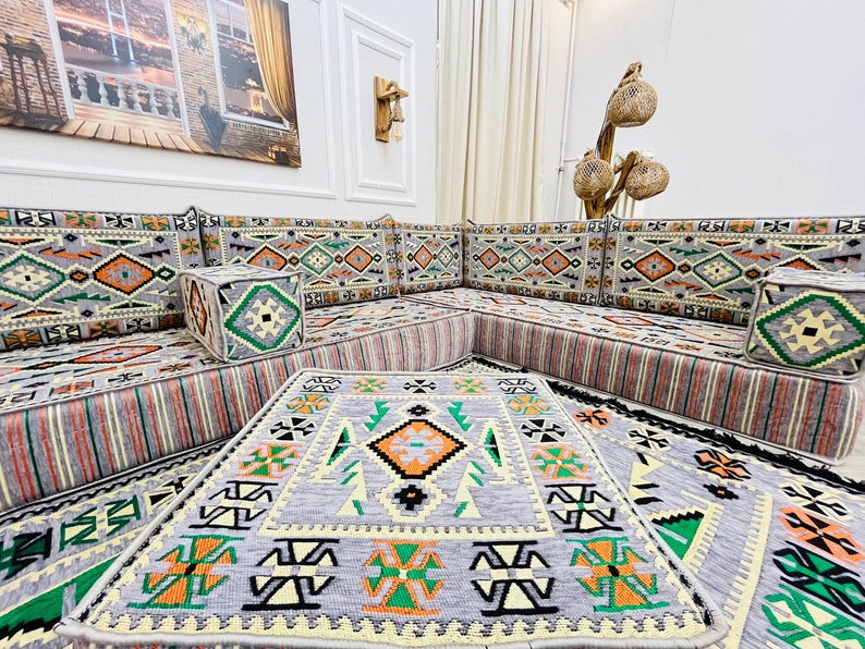May include: A gray and white patterned sectional sofa with orange and green accents. The sofa is made up of multiple cushions and is arranged in a U-shape. There are three gray and white patterned throw pillows on the sofa. The sofa is sitting on a gray and white patterned rug.