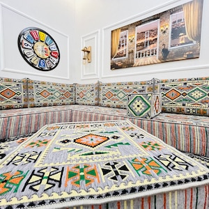 May include: A gray and white patterned floor cushion with orange and green accents. The cushion is part of a larger seating area with multiple cushions and a coffee table.