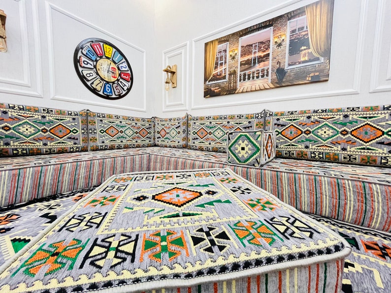 May include: A gray and white patterned floor cushion with orange and green accents. The cushion is part of a larger seating area with multiple cushions and a coffee table.